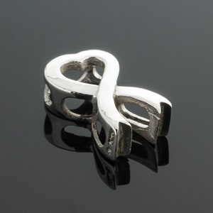 May include: A silver charm in the shape of a heart and infinity symbol. The charm is designed to be worn on a bracelet or necklace.