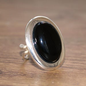 May include: A silver ring with a large oval black onyx stone set in a bezel setting.