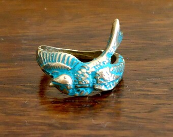 May include: A turquoise blue and gold bird ring. The bird is in flight with its wings spread out. The ring is made of metal and has a detailed design.