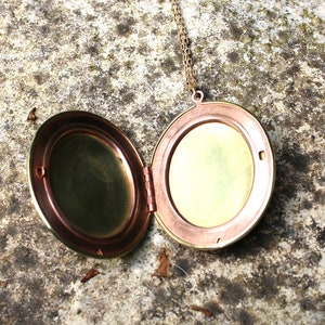 May include: A round, brass locket necklace with a hinged lid. The locket is open, revealing a brass interior.