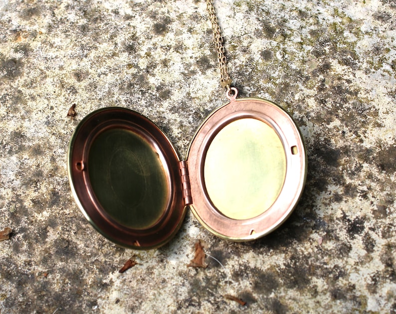 May include: A round, brass locket necklace with a hinged lid. The locket is open, revealing a brass interior.