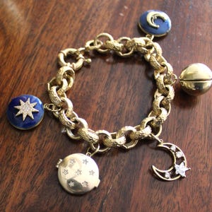 May include: A gold charm bracelet with a variety of charms, including a star, a crescent moon, a locket, and a bell. The charms are all decorated with small diamonds.