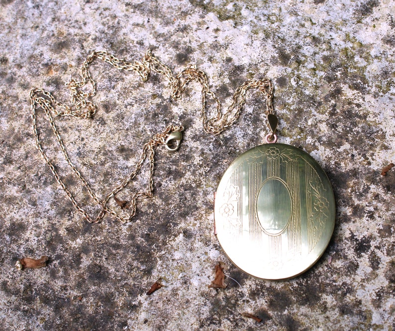 May include: A gold locket necklace with a detailed engraved design. The locket is oval shaped and has a hinged opening. The chain is delicate and has a lobster clasp.