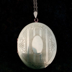May include: A gold oval locket with a chain. The locket has a decorative design of vertical lines and floral motifs.