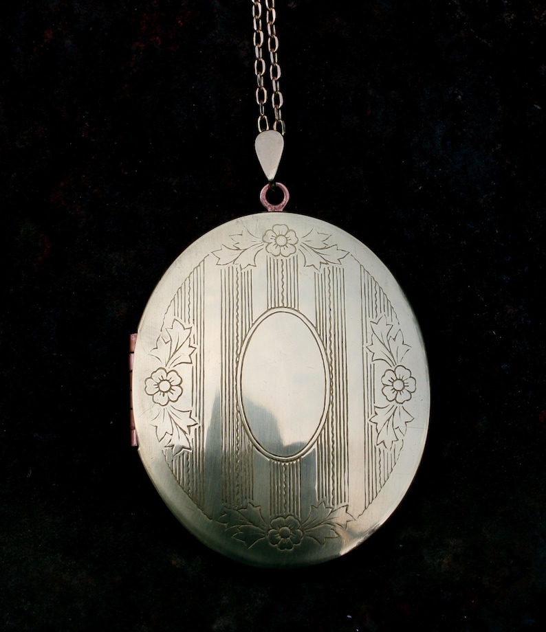 May include: A gold oval locket with a chain. The locket has a decorative design of vertical lines and floral motifs.