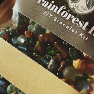 May include: A DIY bracelet kit with the words "rainforest" and "DIY Bracelet Kit" printed on the packaging. The kit contains a variety of beads in shades of green, brown, blue, and orange. The kit is from High Tide Studios.