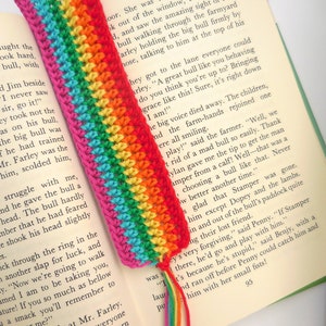 Puede incluir: Un marcap&aacute;ginas de ganchillo arco&iacute;ris con hilo rosa, rojo, naranja, amarillo, verde, azul y morado. El marcap&aacute;ginas est&aacute; colocado en un libro con texto que dice "Ella estaba muy molesta. "Vale, sal por la ventana, Penny," dijo ..."