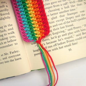 May include: A rainbow crochet bookmark with a tassel. The bookmark is made with different colored yarn, including red, orange, yellow, green, blue, indigo, and violet. The tassel is made with the same colors of yarn.