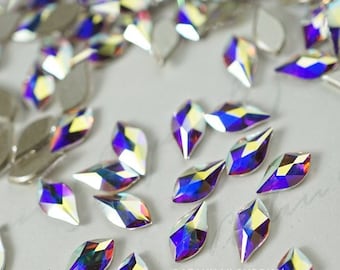 May include: Assortment of iridescent, teardrop-shaped rhinestones with a faceted design. The rhinestones are scattered on a white surface.