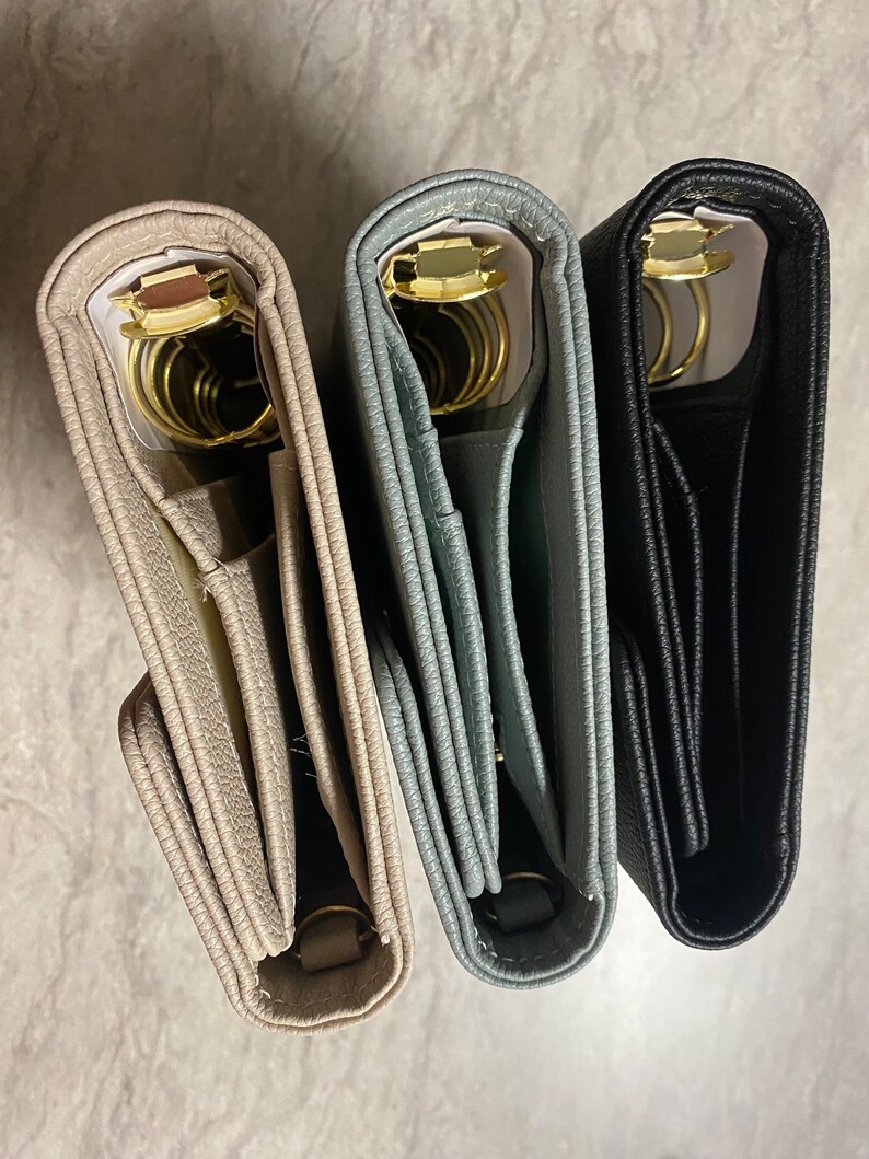 Pode incluir: Tr&ecirc;s di&aacute;rios encadernados em couro nas cores bege, cinza e preto com argolas douradas. Os di&aacute;rios est&atilde;o fechados e empilhados um em cima do outro.
