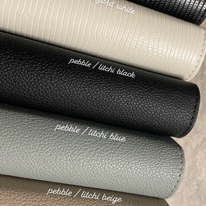 Pode incluir: Cinco amostras de couro de diferentes cores e texturas. As amostras est&atilde;o dispostas em uma pilha, com a amostra superior de couro de lagarto preto, seguida de couro de lagarto branco, couro de seixo preto, couro de seixo azul e couro de seixo bege.