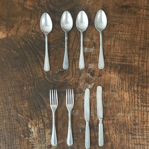 May include: A set of silver cutlery, including spoons, forks, and a butter knife, arranged in a row on a wooden surface.