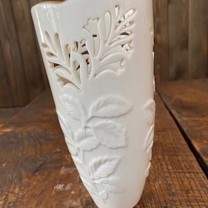 May include: White porcelain vase with a floral design. The vase has a scalloped rim and intricate cutouts.