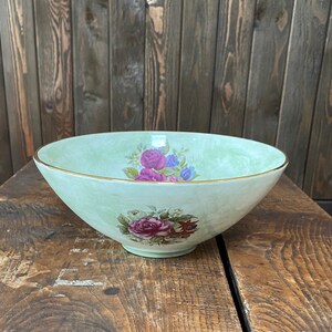 May include: A large, light green ceramic bowl with a gold rim. The bowl is decorated with a floral pattern of pink, purple, and white roses.