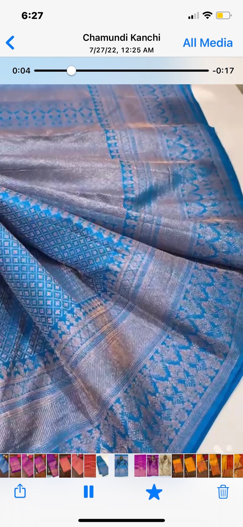 May include: A close-up of a blue and silver silk sari with intricate woven patterns. The fabric has a shimmering quality, with detailed floral and geometric designs. The sari is folded, showcasing its texture and color variations.