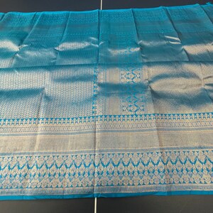 May include: A turquoise textile with intricate silver patterns. The fabric features detailed geometric and floral designs along the borders and central sections. The overall appearance is luxurious and elegant, suitable for apparel or home decor.