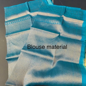 May include: Teal blouse material with a textured weave and decorative border. The fabric is folded, displaying the intricate pattern and the text "Blouse material". The material has a sheen and a soft appearance.