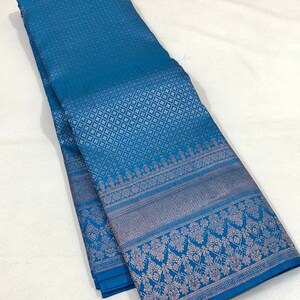 May include: A folded teal textile with a detailed pattern. The fabric has a repeating geometric design across the main body and a decorative border with floral and geometric elements. The textile is likely used for clothing or home decor.