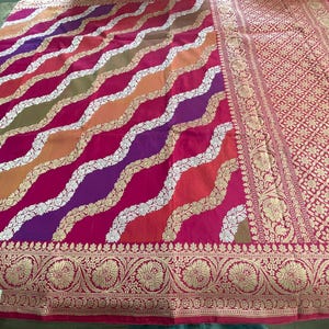 May include: A pink, purple, orange, and green patterned silk saree with a gold and silver border. The saree has a traditional Indian design.