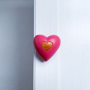 May include: A pink heart-shaped door knob with a gold heart in the centre.