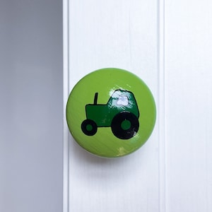 May include: A green round knob with a green tractor design. The tractor has a black outline and black wheels.