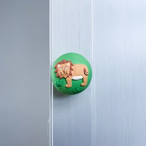 May include: A green round door knob with a brown lion illustration on it. The lion is standing on a green patch of grass.