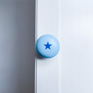 May include: A light blue round cabinet knob with a white polka dot pattern and a blue star in the centre.