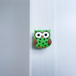 May include: Green owl-shaped door knob with brown wings and black polka dots.