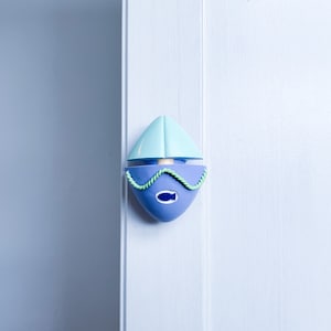 May include: A blue and green plastic toy sailboat with a rope detail. The sailboat is attached to a white door.