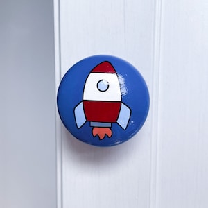 May include: A blue round knob with a red, white and blue rocket ship painted on it.