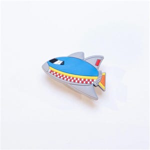May include: A blue and grey toy rocket with red and yellow chequered stripes and a red and orange flame.