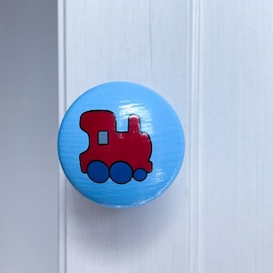 May include: A light blue round wooden knob with a red train painted on it. The train has black wheels and a black window.