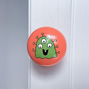May include: A round, orange door knob with a green, three-eyed monster with a smiling face painted on it.