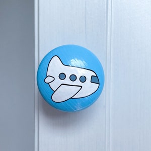May include: A blue round knob with a white airplane painted on it. The airplane has three windows and a black outline.