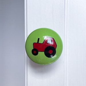 May include: A green round knob with a red tractor design. The tractor has black wheels and a white window.