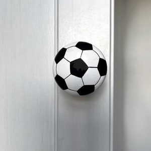 May include: A white and black football door knob. The knob is round and has a black and white pattern.