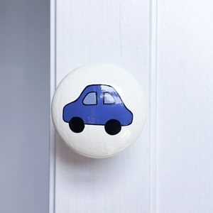 May include: A white round knob with a blue car design. The car has black wheels and a black outline.