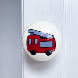 May include: A white round knob with a red fire engine painted on it. The fire engine has a black outline and blue details.