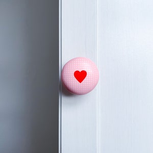 May include: Pink polka dot cabinet knob with a red heart in the centre.