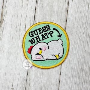 May include: Embroidered patch with a light green background and a yellow border. The patch features a cartoon chicken with the text "GUESS WHAT?" above it. The chicken is white with a red comb and yellow accents.