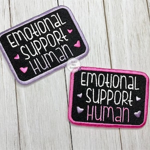 May include: Two embroidered patches with the text "EMOTIONAL SUPPORT HUMAN". One patch has a black background with a purple border, the other has a black background with a pink border. Both have white text and pink heart accents.