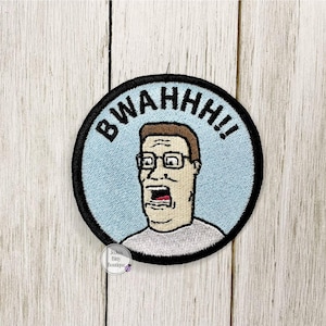 May include: Embroidered patch featuring a cartoon character with glasses and an open mouth, set against a light blue background. The black-bordered patch has the word "BWAHH!!" in black letters. The patch is round and appears to be iron-on.