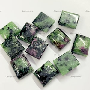 Op de afbeelding: Een verzameling vierkant geslepen edelstenen met een mix van groene en donkerrode tinten. De stenen hebben een gepolijste, glanzende afwerking en zijn gerangschikt op een witte ondergrond. De edelstenen worden waarschijnlijk gebruikt voor het maken van sieraden.