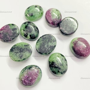 Op de afbeelding: Een verzameling ovaalvormige zoisiet edelstenen met een mix van groene en magenta kleuren. De edelstenen zijn gepolijst en hebben een glad, glanzend oppervlak. Het woord "Gemscount" staat op de afbeelding.