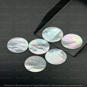 May include: Six iridescent, round mother-of-pearl shell beads. The beads have a pearlescent sheen with hints of pink, green, and blue. They are arranged on a dark surface, with some beads partially on a black tray.