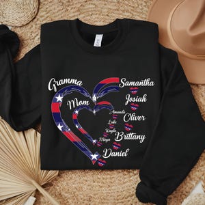 K&ouml;nnte beinhalten: Schwarzes Sweatshirt mit einem Herzdesign in Rot, Wei&szlig; und Blau. Das Herz besteht aus drei ineinander verschachtelten Herzen mit Namen wie "Gramma", "Mom", "Samantha" und "Josiah" in wei&szlig;er Schrift. Ein personalisiertes, gem&uuml;tliches Geschenk.