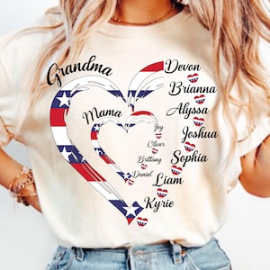 K&ouml;nnte beinhalten: Cremefarbenes T-Shirt mit herzf&ouml;rmigem Design in Rot, Wei&szlig; und Blau. Die W&ouml;rter "Grandma" und "Mama" sind abgebildet, zusammen mit Namen wie Devon und Brianna. Das Design hat ein patriotisches Thema.