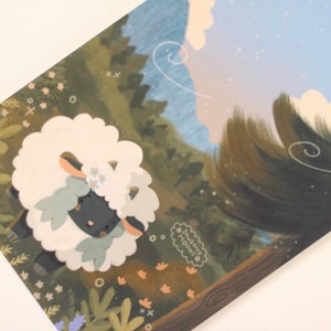 Pu&ograve; includere: Una pecora nera con un mantello bianco e soffice e fiori blu nei capelli si trova in una foresta verde con un cielo blu e nuvole bianche sullo sfondo. Il testo "dreamy moodi" &egrave; scritto in un cerchio bianco.
