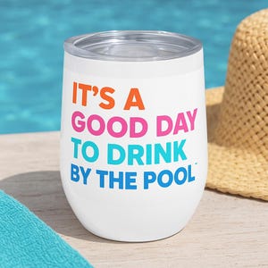 May include: White stemless wine tumbler with a clear lid. The tumbler has the text "IT'S A GOOD DAY TO DRINK BY THE POOL" in orange, pink, teal, and blue. A straw hat is in the background.