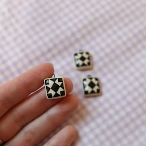 May include: Three white ceramic charms with black geometric patterns. Each charm has a small loop for attaching to a necklace or bracelet.